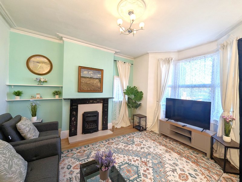 Bright living room with mint green accent wall, fireplace, grey sofa, TV, and large windows