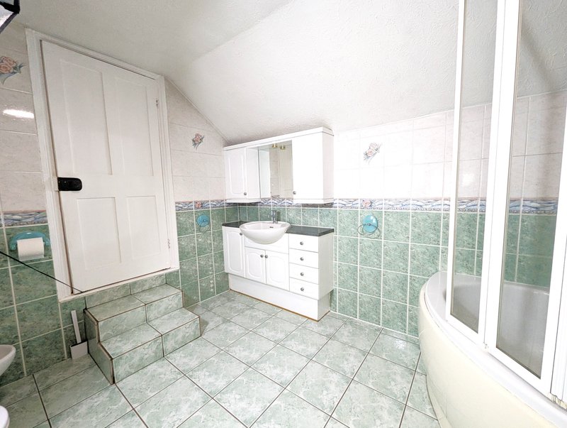 Bright bathroom with green tile walls, white vanity, bathtub and sloped ceiling