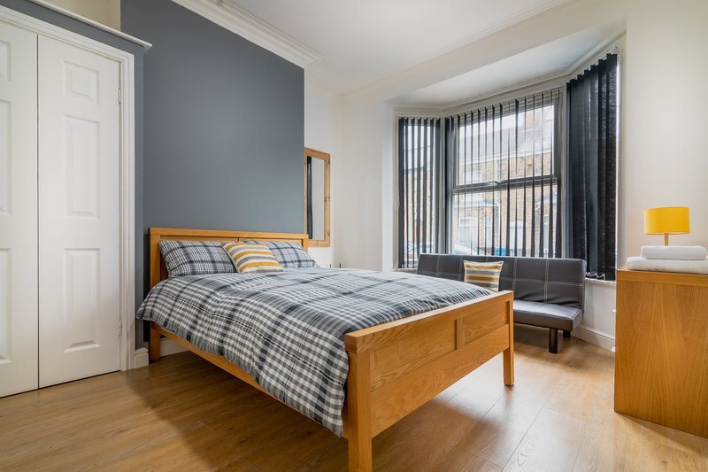 Bright bedroom with wooden bed, blue plaid bedding, feature wall, and large windows with dark curtains
