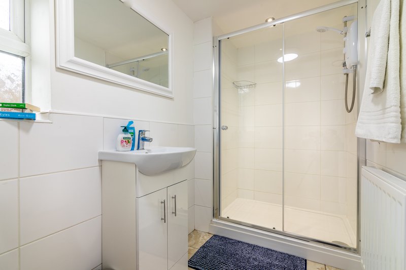 Modern bathroom with white tiles, wall-mounted sink, mirror, shower enclosure and blue bath mat