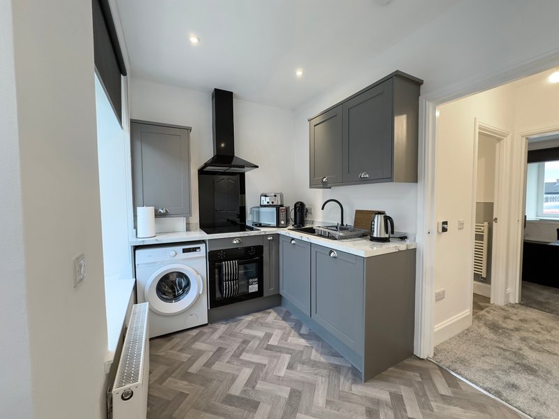 Modern kitchen with grey cabinetry, black cooker hood, washing machine, and herringbone flooring