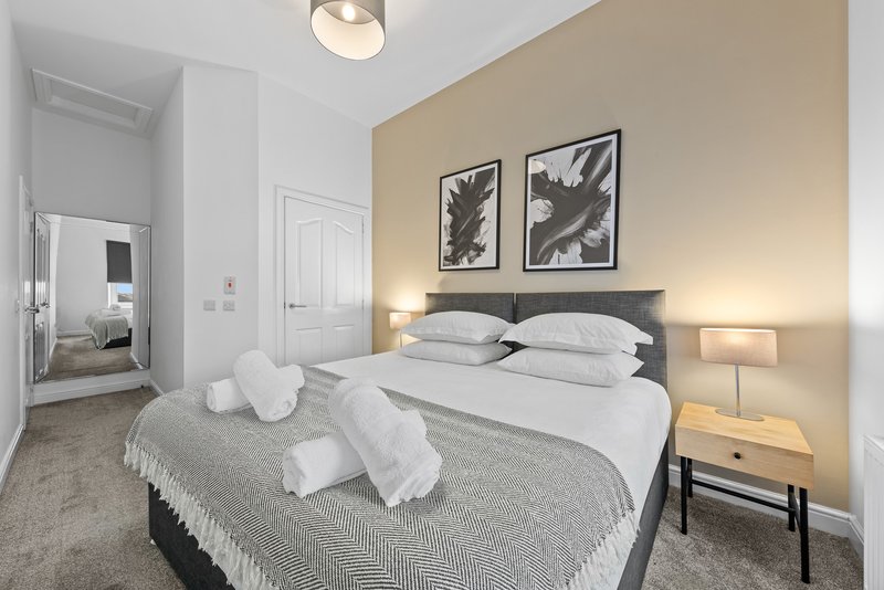 Modern bedroom with double bed, white pillows, grey bedding, and two framed botanical prints on wall