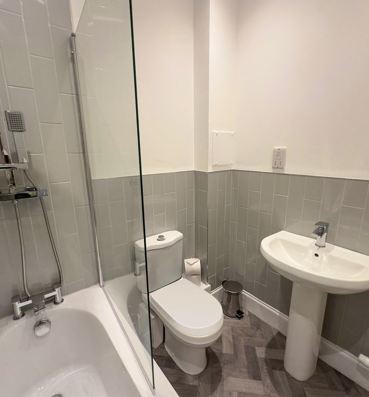 Modern bathroom with bathtub, toilet, pedestal sink and tiled walls