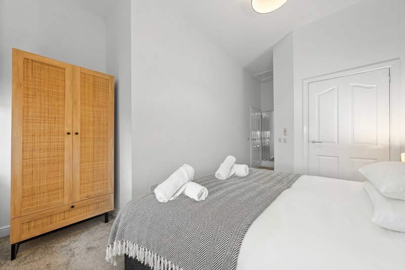 Modern bedroom with double bed, wooden wardrobe, white pillows and grey bedding
