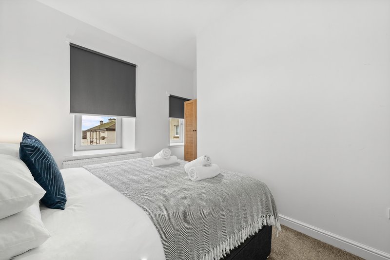 Bright bedroom with two single beds, grey bedding, blue cushion, and window with roller blind