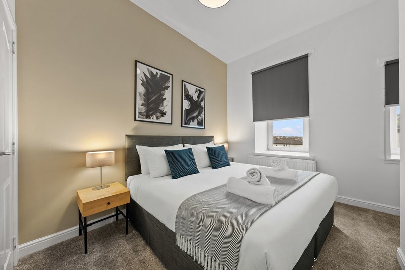 Modern bedroom with double bed, bedside lamp, artwork, and window with blind