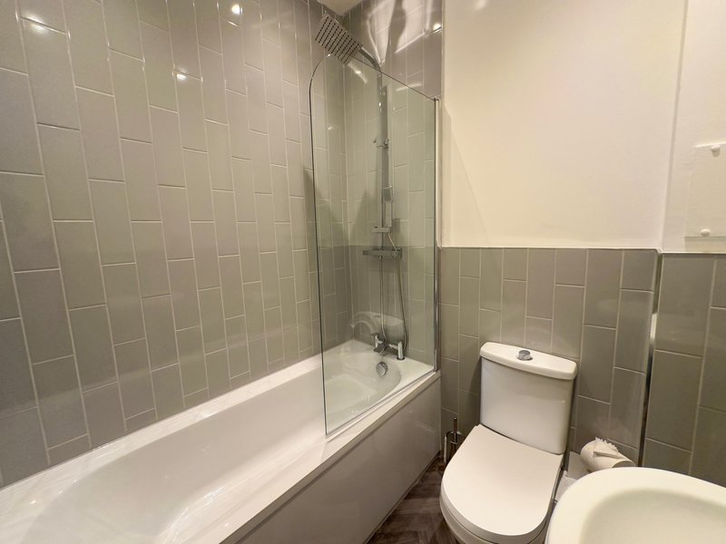 Modern bathroom with grey subway tiles, white bathtub, glass shower screen and toilet