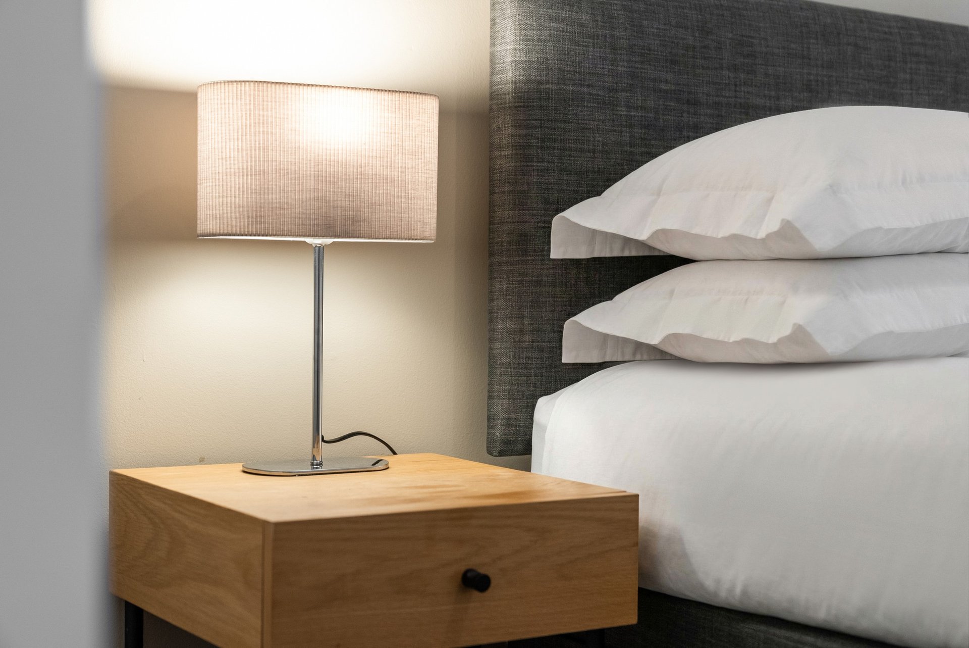 Bedroom nightstand with table lamp next to bed with white pillows