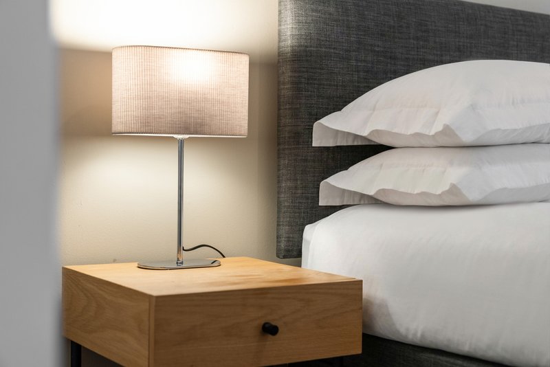 Bedroom nightstand with table lamp next to bed with white pillows