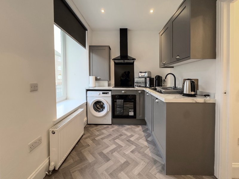 Modern kitchen with grey cabinets, washing machine, black cooker hood and herringbone flooring
