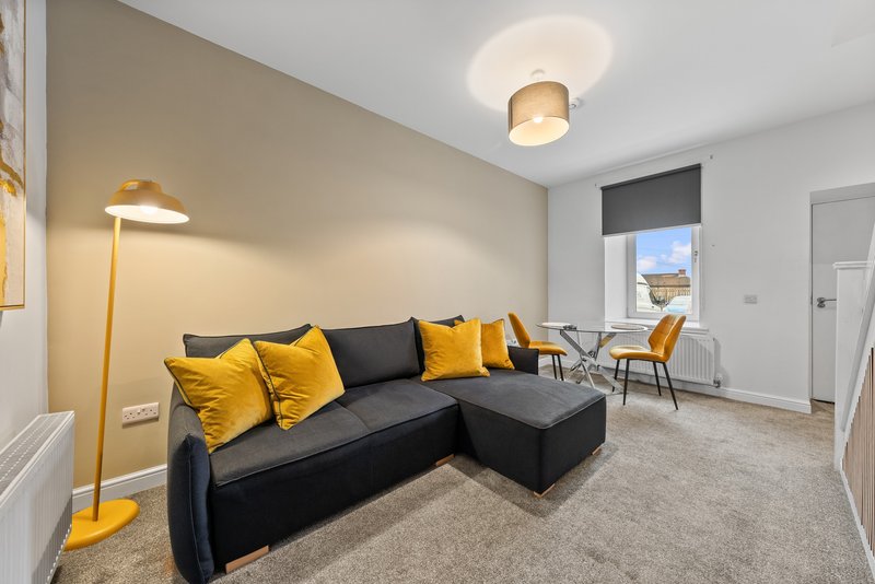 Modern living room with black corner sofa, yellow cushions, floor lamp and window with blinds