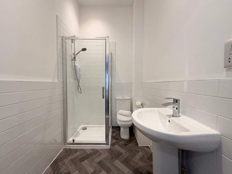 Modern bathroom with walk-in shower, white sink, toilet, and herringbone tile flooring