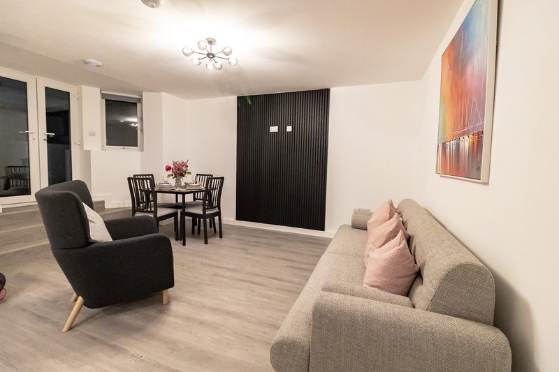 Open-plan living area with grey sofa, black armchair, dining table and abstract wall art