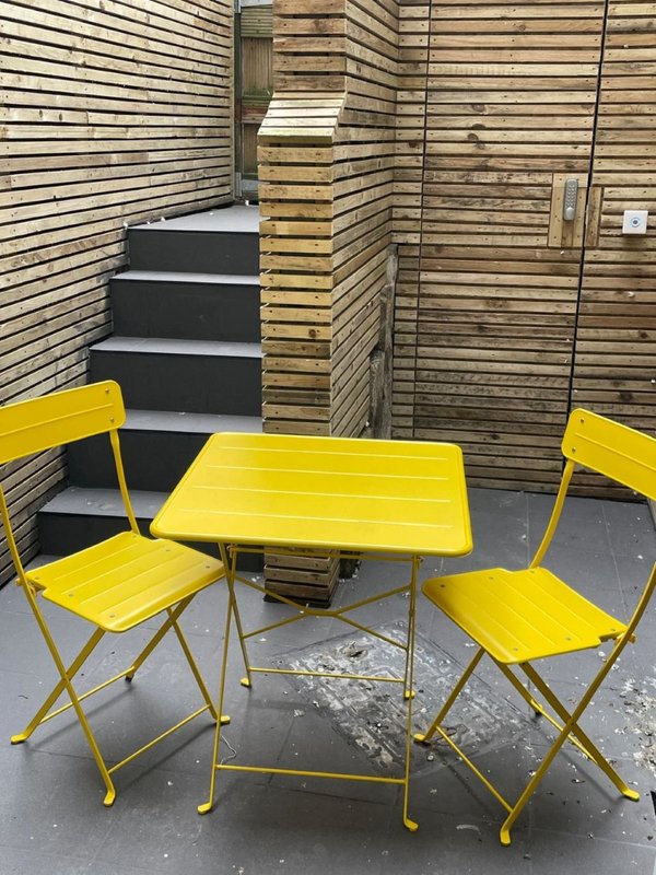 Outdoor patio area with yellow folding table and chairs, wooden fence backdrop