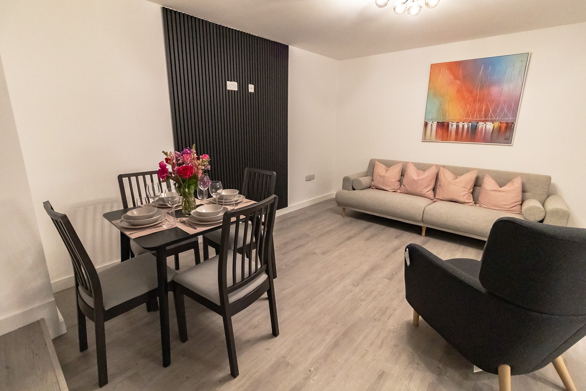 Open-plan living space with dining table, sofa, armchair and abstract wall art