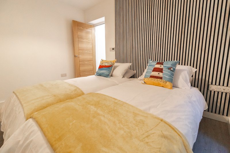 Modern bedroom with two beds, yellow bedding, striped wall paneling and wooden door