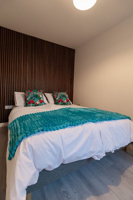 Modern bedroom with double bed, teal bedspread, decorative cushions, and wooden wall paneling