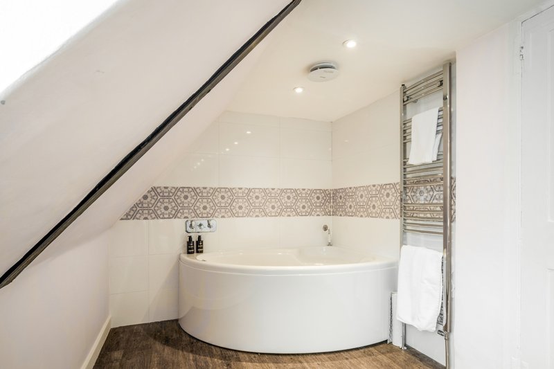 Modern bathroom with white corner bathtub, mosaic tile border, heated towel rail and recessed lighting