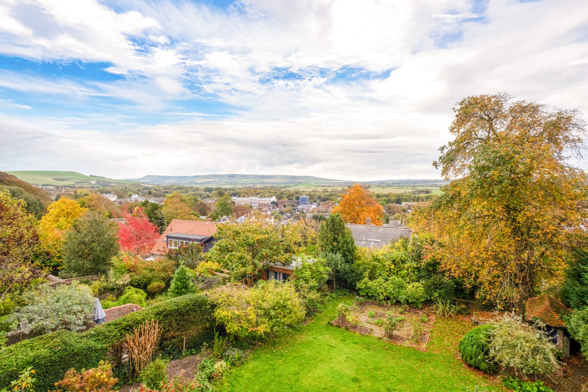 Aerial view of countryside property with garden, trees in autumn colours and distant village landscape