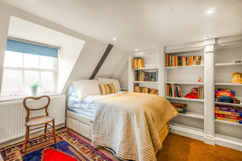 Bright attic bedroom with single bed, built-in bookshelves, window seat and colourful rug
