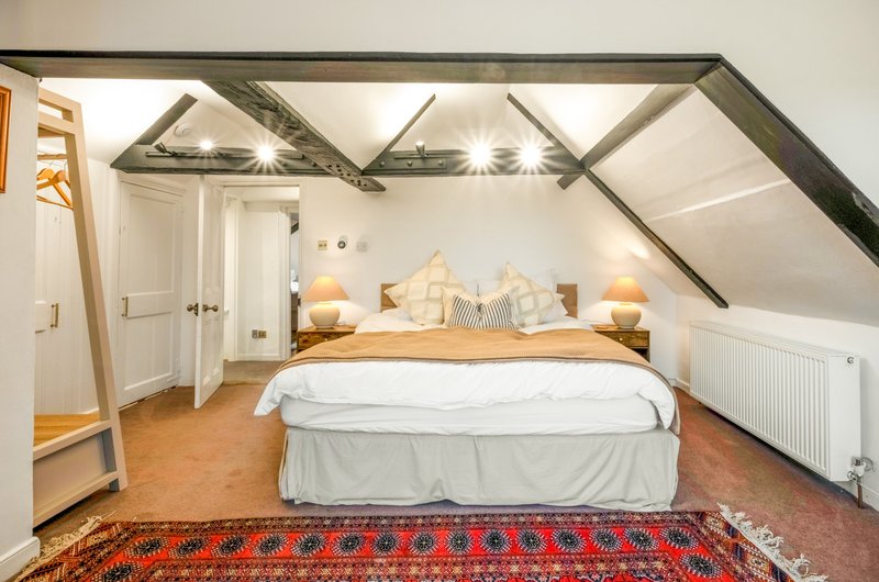 Attic bedroom with sloped ceilings, double bed, wooden floor and traditional rug