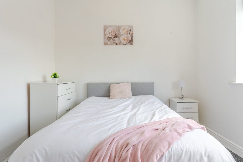 Bright bedroom with double bed, grey headboard, white bedding, pink throw and matching wall art