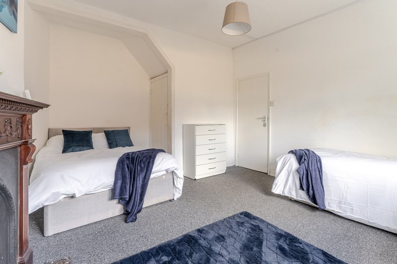 Bright bedroom with two single beds, white bedding, blue throws, and gray carpet flooring
