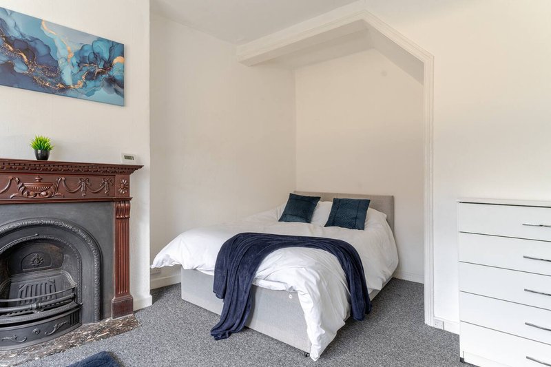 Bedroom with double bed, decorative fireplace, artwork and small plant on mantel