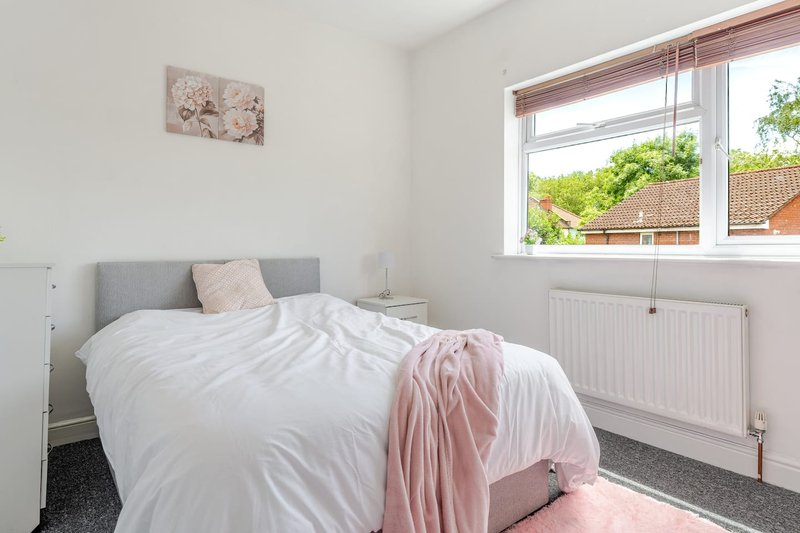 Bedroom with grey headboard, white bedding, pink throw, and large window overlooking garden