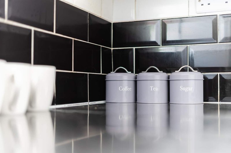 Modern kitchen with black subway tile backsplash, white countertop, and labeled storage canisters