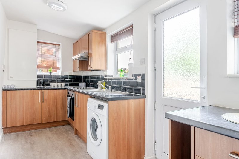 Modern kitchen with wooden cabinets, black tile backsplash, washing machine and patio door