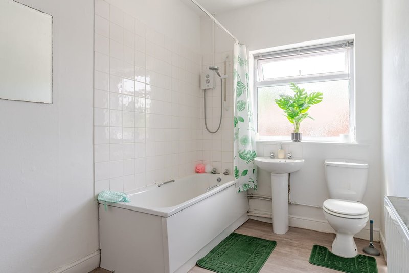 Clean white bathroom with bathtub, toilet, pedestal sink and window with plants
