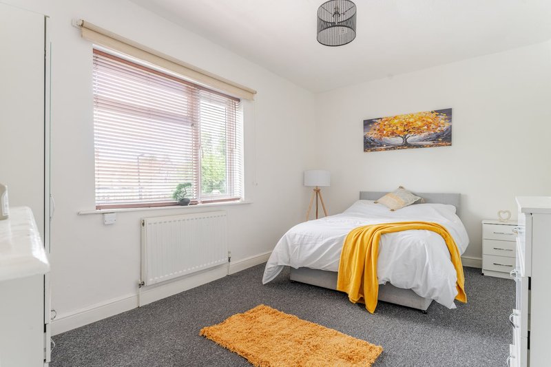 Bright bedroom with double bed, grey carpet, yellow throw blanket and matching rug