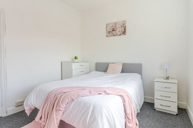 Bright bedroom with double bed, pink throw, grey headboard, white bedside tables and wall art