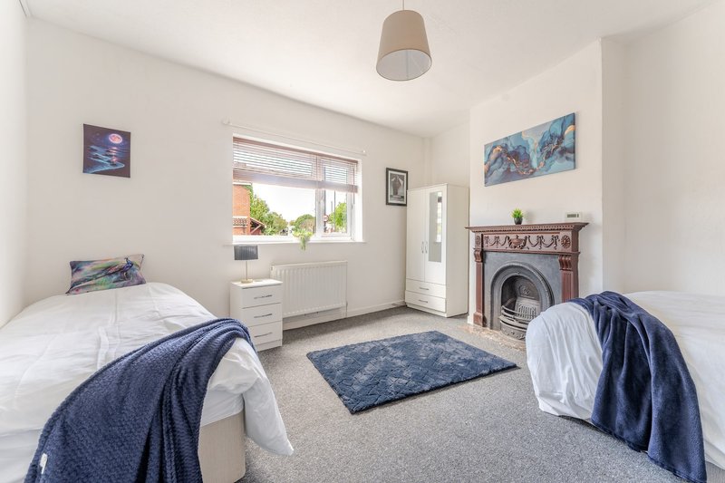 Bright bedroom with two single beds, fireplace, window and neutral decor