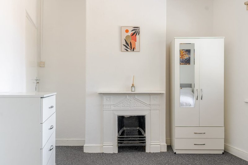 Bright living room with white fireplace, small framed artwork, cream storage cabinet and modern wardrobe