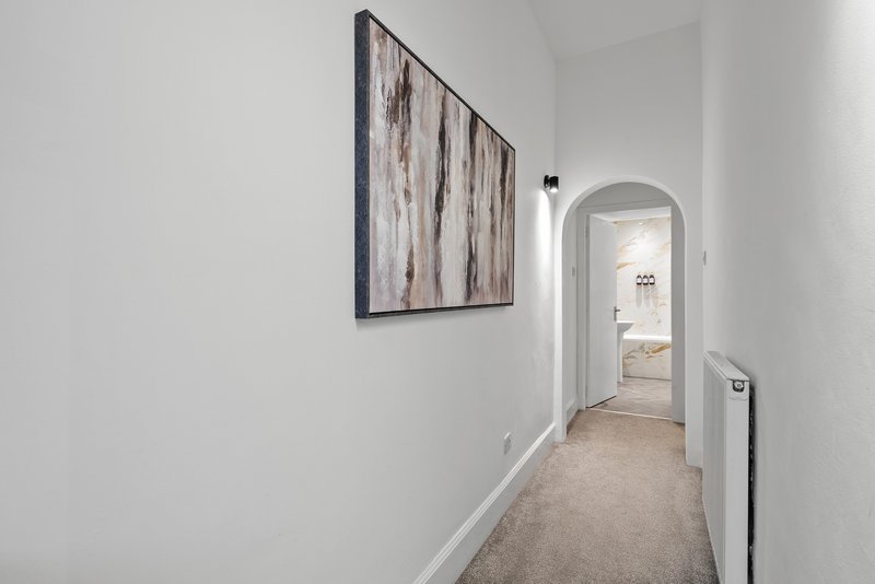 Neutral hallway with framed artwork, white walls, carpeted floor and doorway