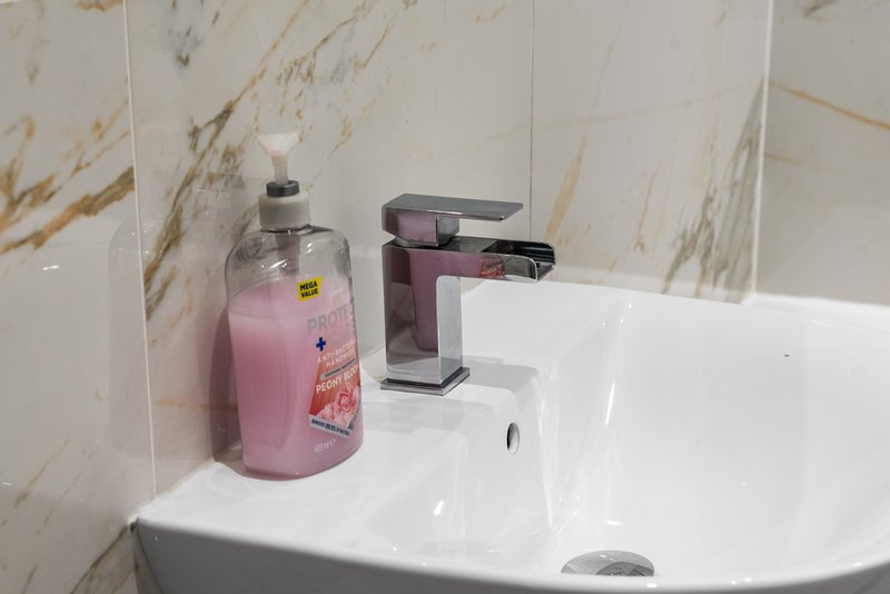 Bathroom sink with marble-effect tiling, pink soap dispenser, and modern tap fixture