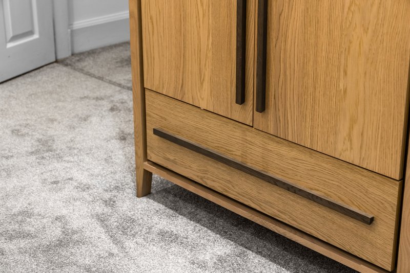 Modern wooden cabinet with black handles on light grey carpeted floor