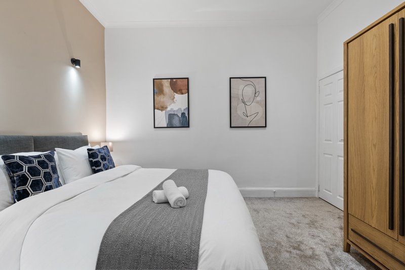 Modern bedroom with double bed, grey bedding, patterned pillows, wooden wardrobe and framed wall art