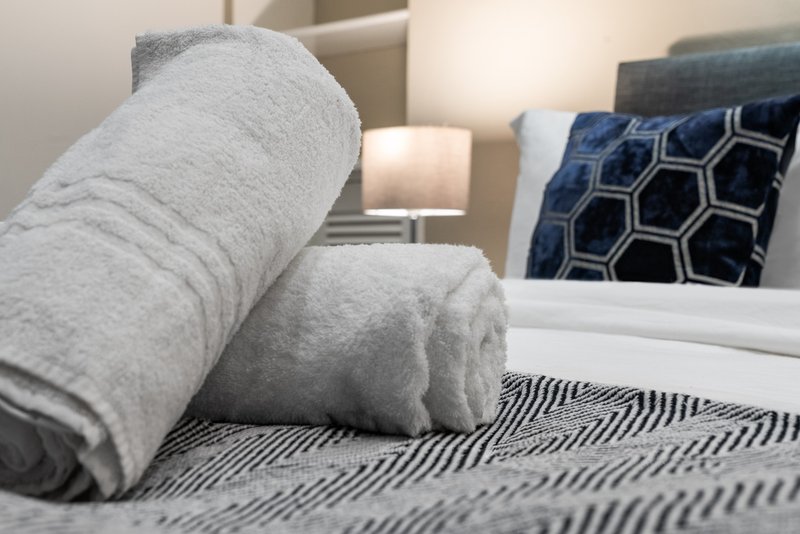 Bed with grey rolled towels, patterned cushions and striped bedding in modern bedroom