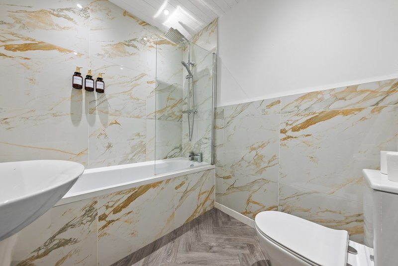 Modern bathroom with marble-effect tiling, glass shower enclosure, white basin and toilet