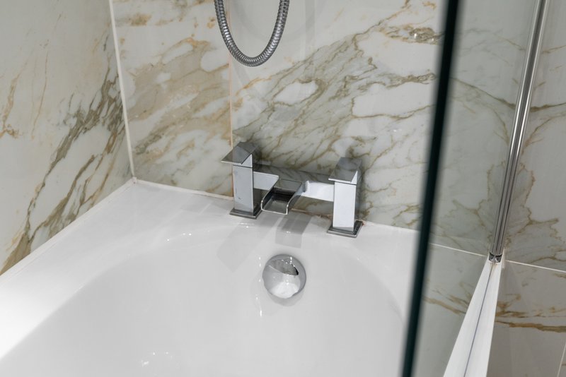 Modern bathroom with marble-effect tiled walls, white bathtub and chrome faucet