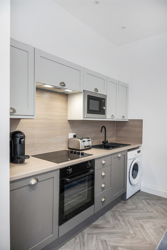 Modern kitchen with grey cabinetry, built-in oven, black sink and countertops