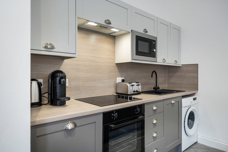 Modern kitchen with white cabinetry, black countertop, built-in appliances and washing machine