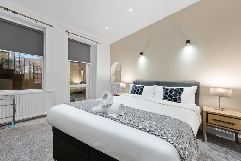 Modern bedroom with double bed, gray bedding, patterned pillows, and wall-mounted lights