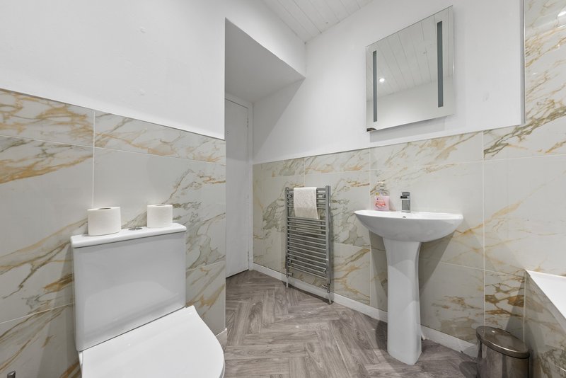 Modern bathroom with pedestal sink, toilet, marble-effect tiles and heated towel rail