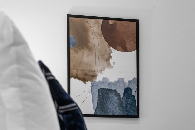 Framed abstract watercolor artwork on white wall with blurred foreground object