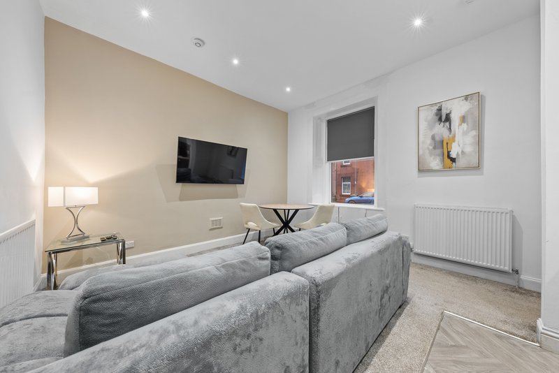 Modern living room with gray corner sofa, wall-mounted TV, lamp and framed artwork