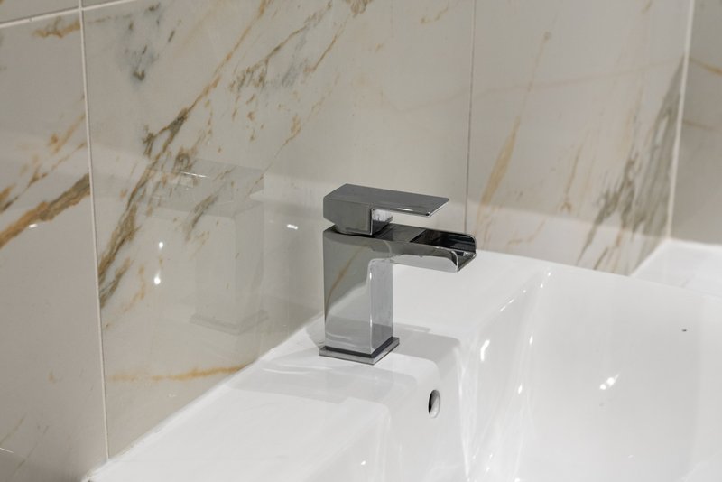 Modern bathroom sink with chrome waterfall faucet and marble-effect tiled wall